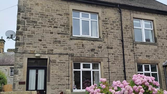 Stone cottage with a cozy appearance, featuring pink hydrangeas and a wooden gate in Langcliffe, Yorkshire.