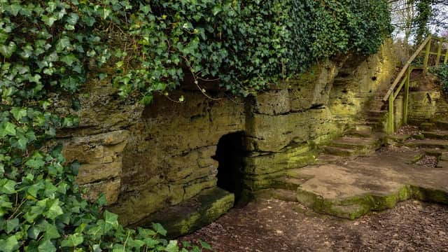 St Robert's Cave features a stone entrance surrounded by lush greenery and steps leading up the hillside.