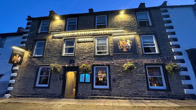 The Kings Arms Hotel in Reeth, Yorkshire, with illuminated signage and flower baskets on a stone facade at dusk.