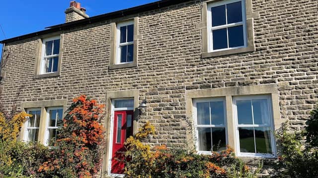 Stone cottage with red door, surrounded by colorful flowers and greenery, under a clear blue sky in Yorkshire.