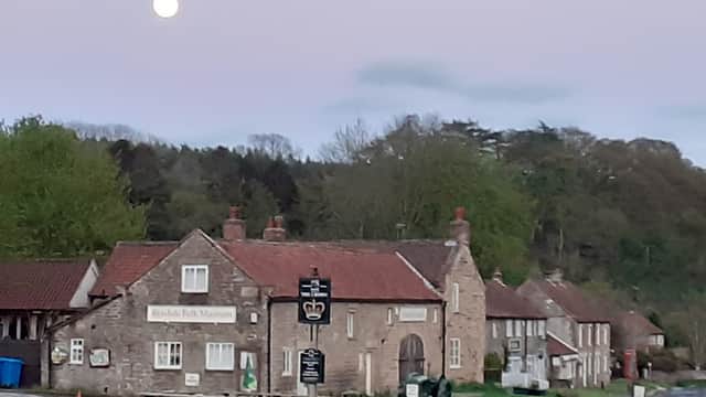 Ryedale Folk Museum building with stone walls, a sign, and outdoor seating, set against a twilight sky and trees.