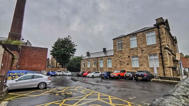 Morley Library Car Park with several parked cars, a stone building, and a cloudy sky in Tingley, Yorkshire.