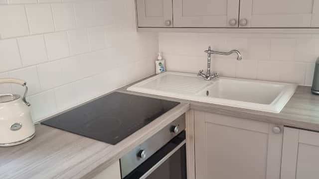 Modern kitchen with white cabinetry, sink, electric stove, and oven, featuring light-colored countertops and tiled floor.