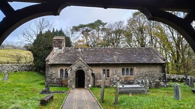 St Leonard's Church features a stone exterior, arched entrance, gravestones, and surrounding trees in a serene landscape.