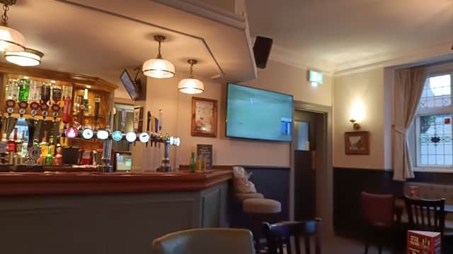 Interior of a cozy bar with a wooden counter, beer taps, a TV screen, and seating areas.