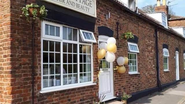 Brick building with large windows, "The Cottage Hair & Beauty" sign, and decorative balloons outside.