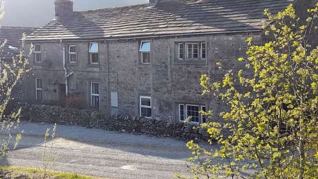 Stone cottage surrounded by greenery, gravel driveway, and scenic hills in the background, located in Starbotton, Yorkshire.