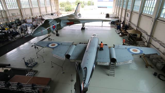 Two vintage military aircraft in a large hangar, with technicians working and equipment scattered around.
