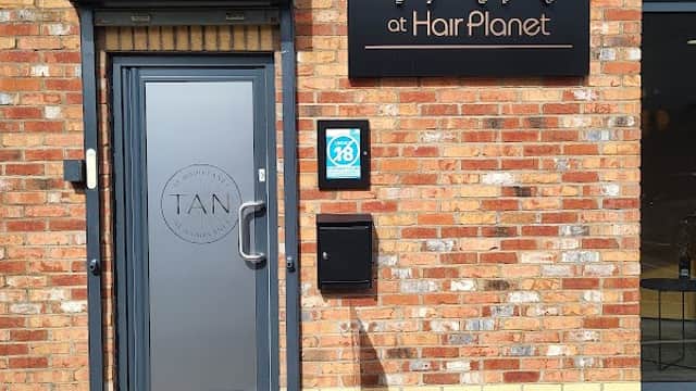 Entrance to TAN at Hair Planet, featuring a stylish door, brick wall, and sign with sunburst design.