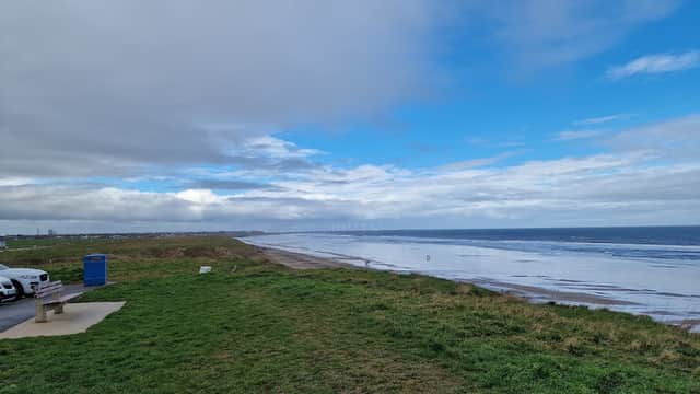 Coastal view from a grassy area with a car park, featuring a cloudy sky and distant shoreline along Marske.