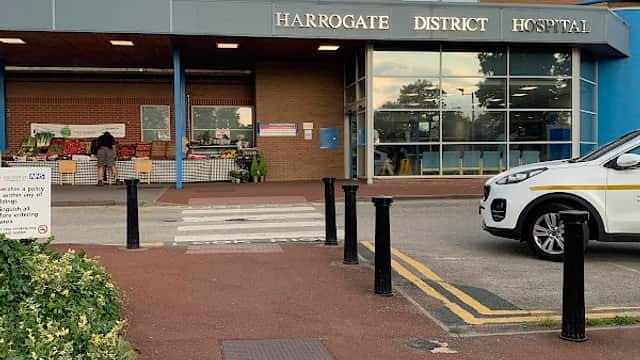 Harrogate District Hospital entrance with a blue facade, sign, and parked cars, surrounded by greenery.