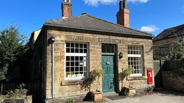 Stone building with a green door, large windows, a red post box, and chimney stacks under a blue sky.