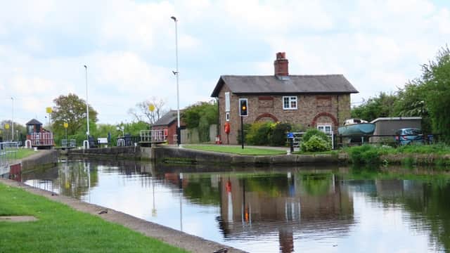 Pollington Village Hall beside a calm canal, surrounded by greenery and blue sky with fluffy clouds.