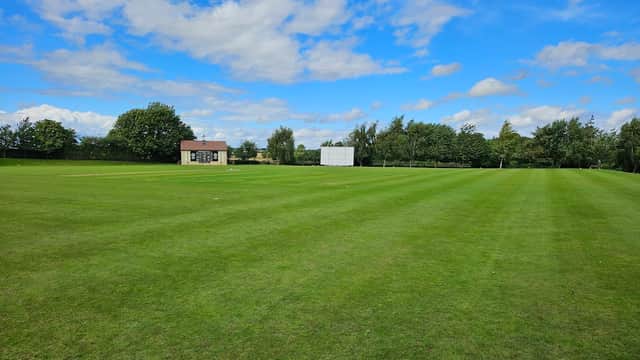 Cricket field with a clubhouse and scoreboard under a blue sky with scattered clouds in Saxton, North Yorkshire.