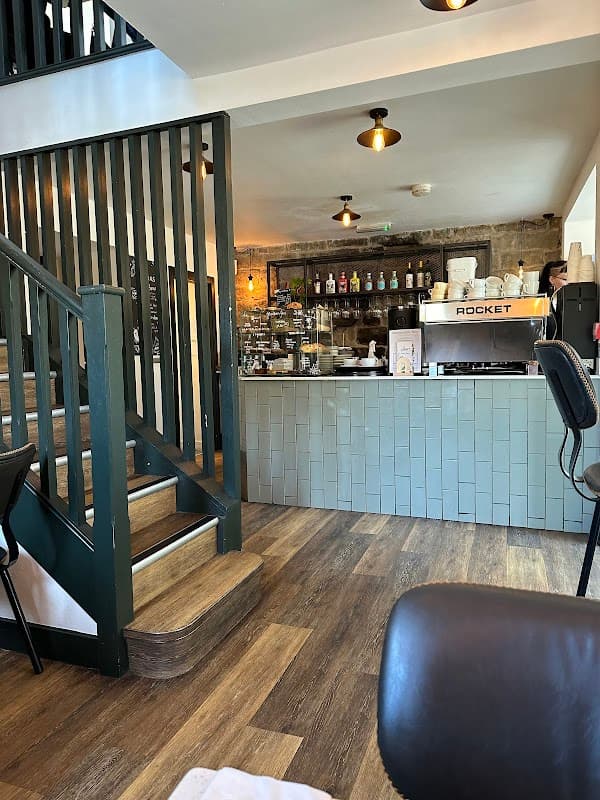 Cozy interior of Joni Grocers with a coffee machine, shelves of goods, and a staircase leading to the upper level.