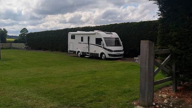 A white caravan parked on a grassy area, surrounded by tall hedges and a cloudy sky in Thornthorpe Caravan Site.