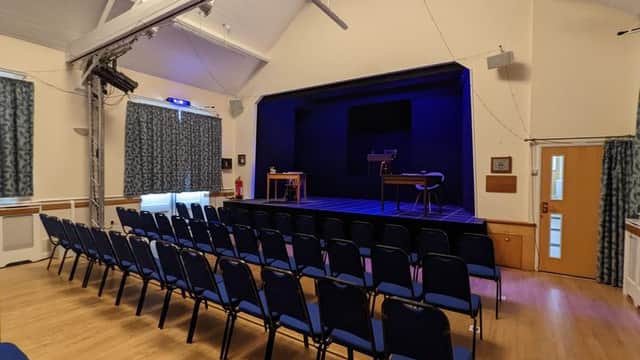 Interior of Robinson Institute Village Hall with rows of blue chairs facing a stage and blue lighting.