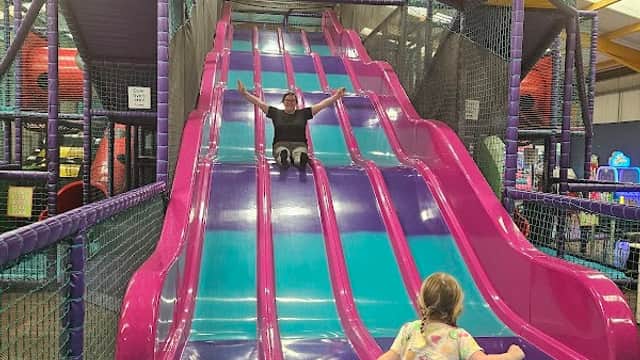 Colorful indoor slide with children playing; one slides down while another stands at the bottom, excited.