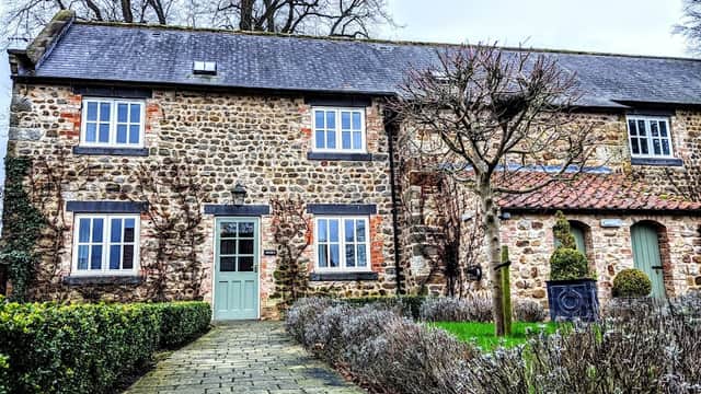 Charming stone hotel with green door, surrounded by trimmed hedges and trees, in a serene Yorkshire setting.
