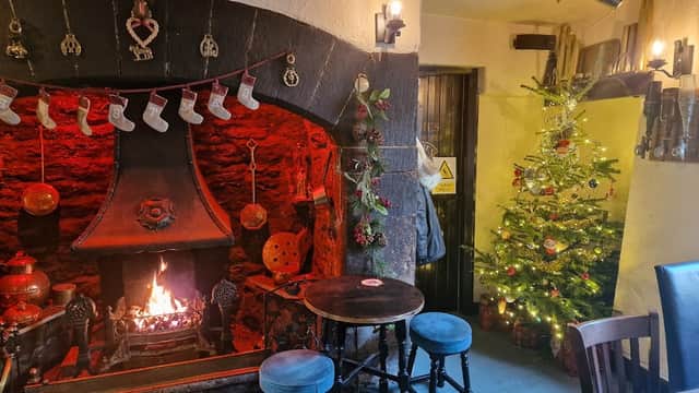 Cozy bar interior with a stone fireplace, festive decorations, a Christmas tree, and wooden tables and chairs.