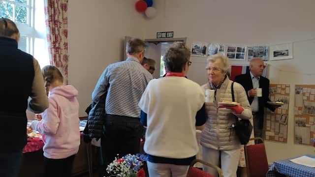 People interacting in a community room with tables, floral arrangements, and historical photos on the walls.