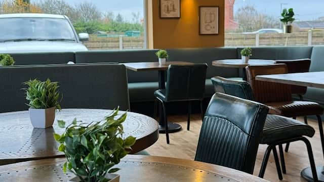 Cozy bistro interior with wooden tables, green plants, and pendant lights, overlooking a scenic view.