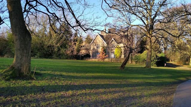 Lush green park with bare trees, a historic stone building, and a winding path under a clear blue sky.