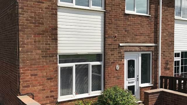 Brick house with white windows and a front garden, located in Whitby, North Yorkshire. Clear blue sky above.