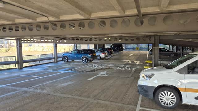 Multi-level car park with parked vehicles and a "Give Way" sign visible on the ground. Bright, open space.