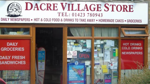 Dacre Village Store storefront with signs for groceries, sandwiches, hot drinks, and an "OPEN" notice.