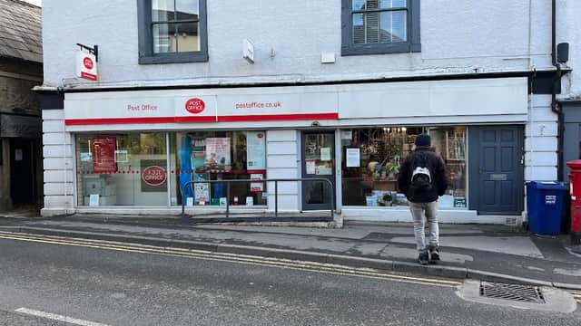 Settle Post Office with a red and white sign, large windows, and a person walking by on a quiet street.