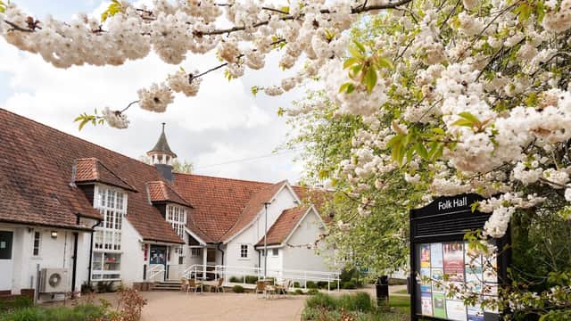Blossoming cherry trees frame the charming New Earswick Folk Hall, showcasing its distinctive architecture and inviting entrance.