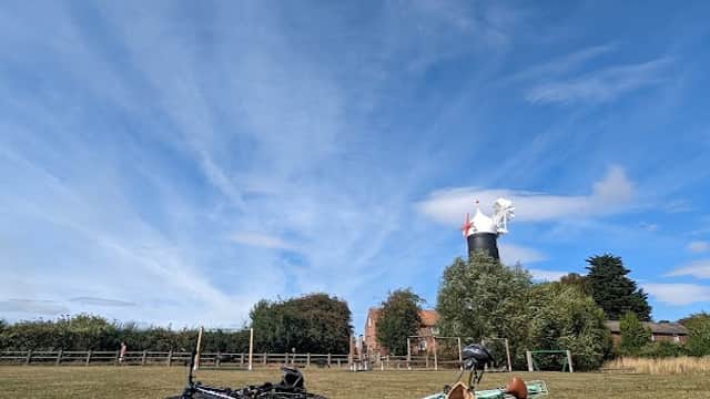 Bicycles and playground equipment on grassy field with blue sky and distant windmill in Skidby, Yorkshire.