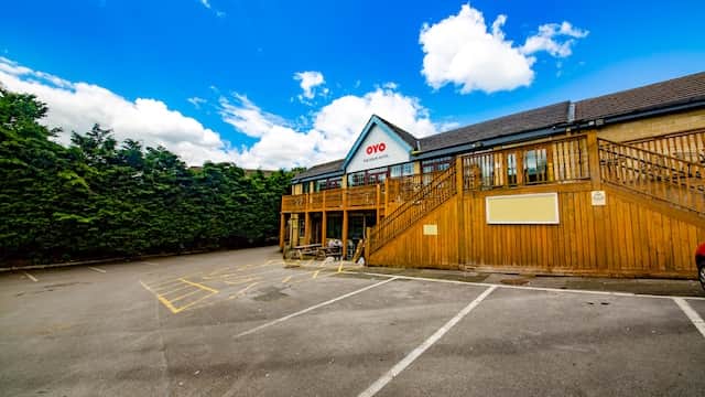 OYO The Rock Hotel with wooden deck, surrounded by greenery and a clear blue sky, in Holywell Green, Yorkshire.