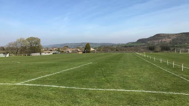 Green football pitch with goalposts, surrounded by trees and hills under a clear blue sky in Hepworth, Yorkshire.