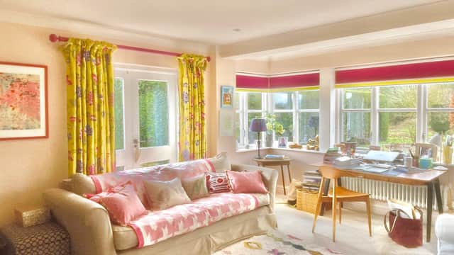 Bright living room with floral curtains, a cozy sofa, a colorful rug, and a desk by large windows.