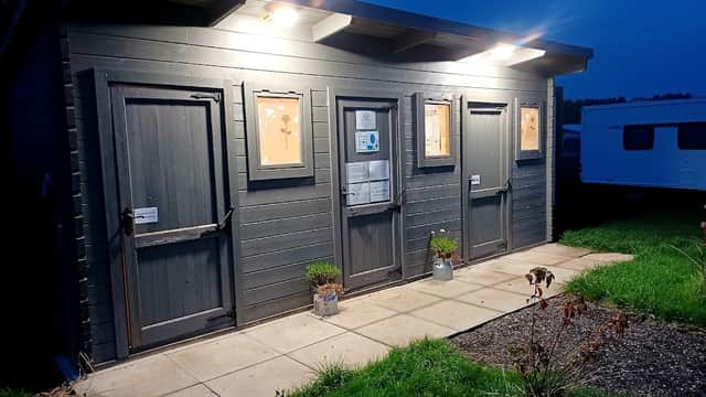 Three dark wooden doors with illuminated signage, set against a twilight sky, surrounded by grass and a gravel path.