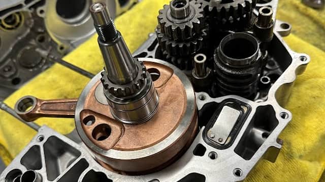 Engine components, including gears and a shaft, arranged on a yellow cloth with tools in the background.