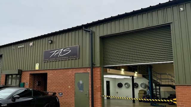 TAS Auto Centre LTD shopfront with a green exterior, garage door, and a black car parked outside.