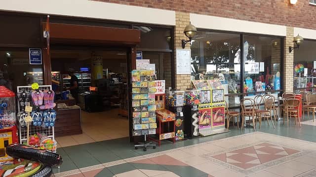 Entrance to Skirlington Supermarket with displays of snacks, toys, and beach items, alongside seating area and checkout.