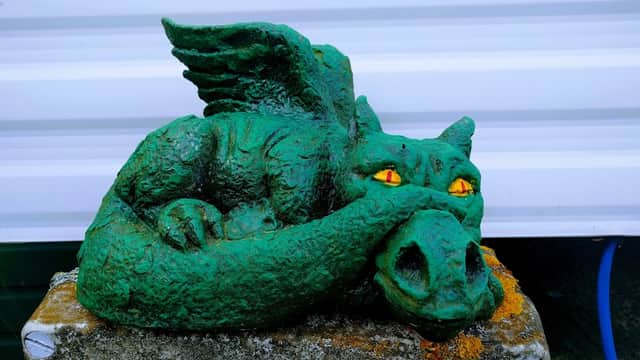 A green dragon statue with wings and glowing orange eyes resting on a stone pedestal at Barcourt Estate Caravan Park.