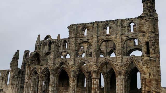 Ruins of Whitby Abbey with stone arches and towers, set against a cloudy sky and grassy foreground.