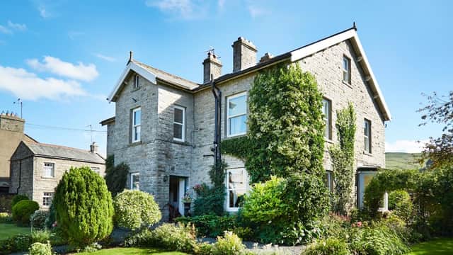 Victorian stone house with ivy, surrounded by a lush garden and bright blue sky in Hawes, Yorkshire.