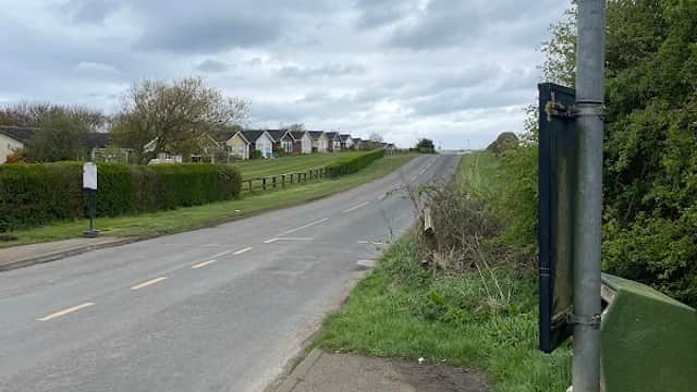 Bus stop sign beside a quiet road in Lebberston, Yorkshire, with houses visible in the distance under a cloudy sky.