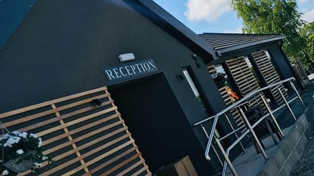 Modern bar venue with wooden slatted exterior, sign reading "RECEPTION," and a clear blue sky above.