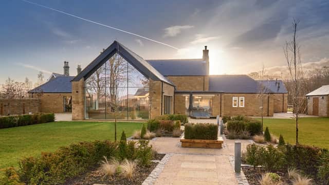 Modern building with a sloped roof, large glass windows, surrounded by landscaped gardens and a stone pathway.