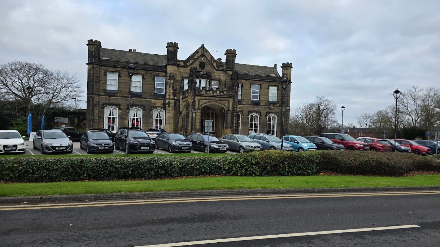 Victorian-style community hall with stone façade, large windows, and a landscaped front lawn, surrounded by parked cars.