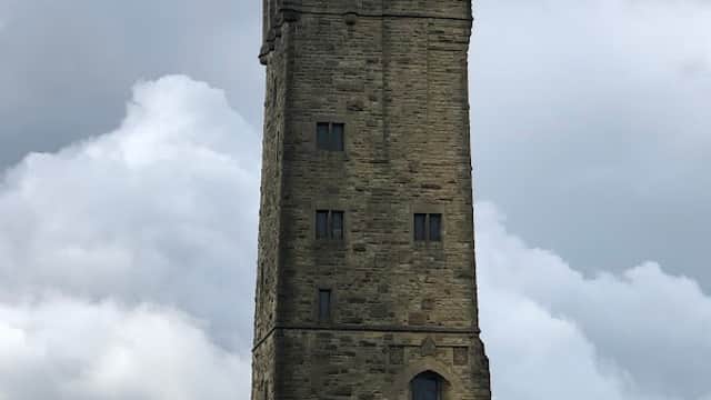 Tall stone tower atop a grassy hill under a cloudy sky, with steps leading to the entrance.
