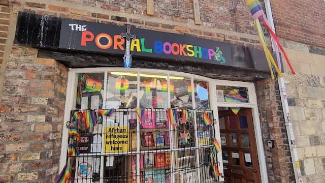 Colorful flags adorn the exterior of The Portal Bookshop, showcasing a vibrant window display of books.