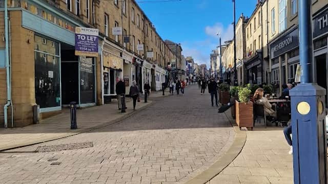 Bustling street scene with shops, pedestrians, and blue sky in Huddersfield, Yorkshire.